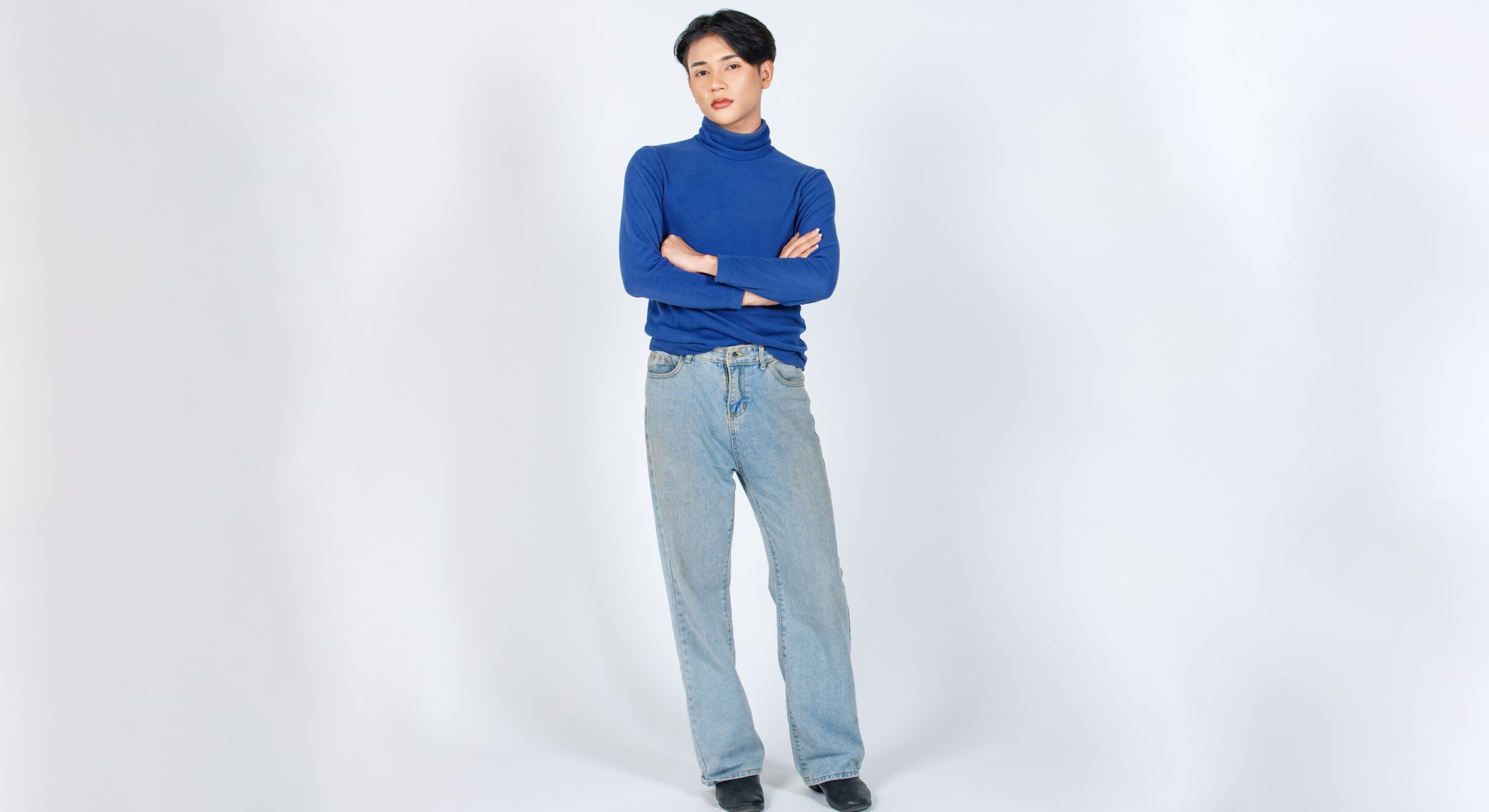 Person in blue turtleneck and light jeans standing.