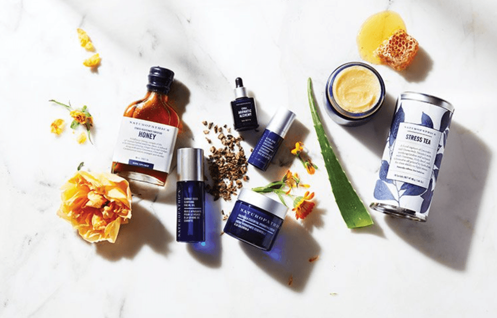 Naturopathica products on a marble countertop surrounded by flowers and an aloe leaf